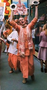 Cymbals aloft, Hare Krishna chanter leaps along Parisian thoroughfare. Paris, France. 1975.