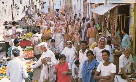 Beaming devotees chant Hare Krishna as they weave their way through one of Vrindavan's colorful bazaars. 1976.