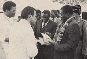 Prime Minister R . C. Mugabe (right) receives Srila Prabhupada's books from Harare temple president Devarsi dasa, as Srinatha Cakravarti dasa (far left) looks on.